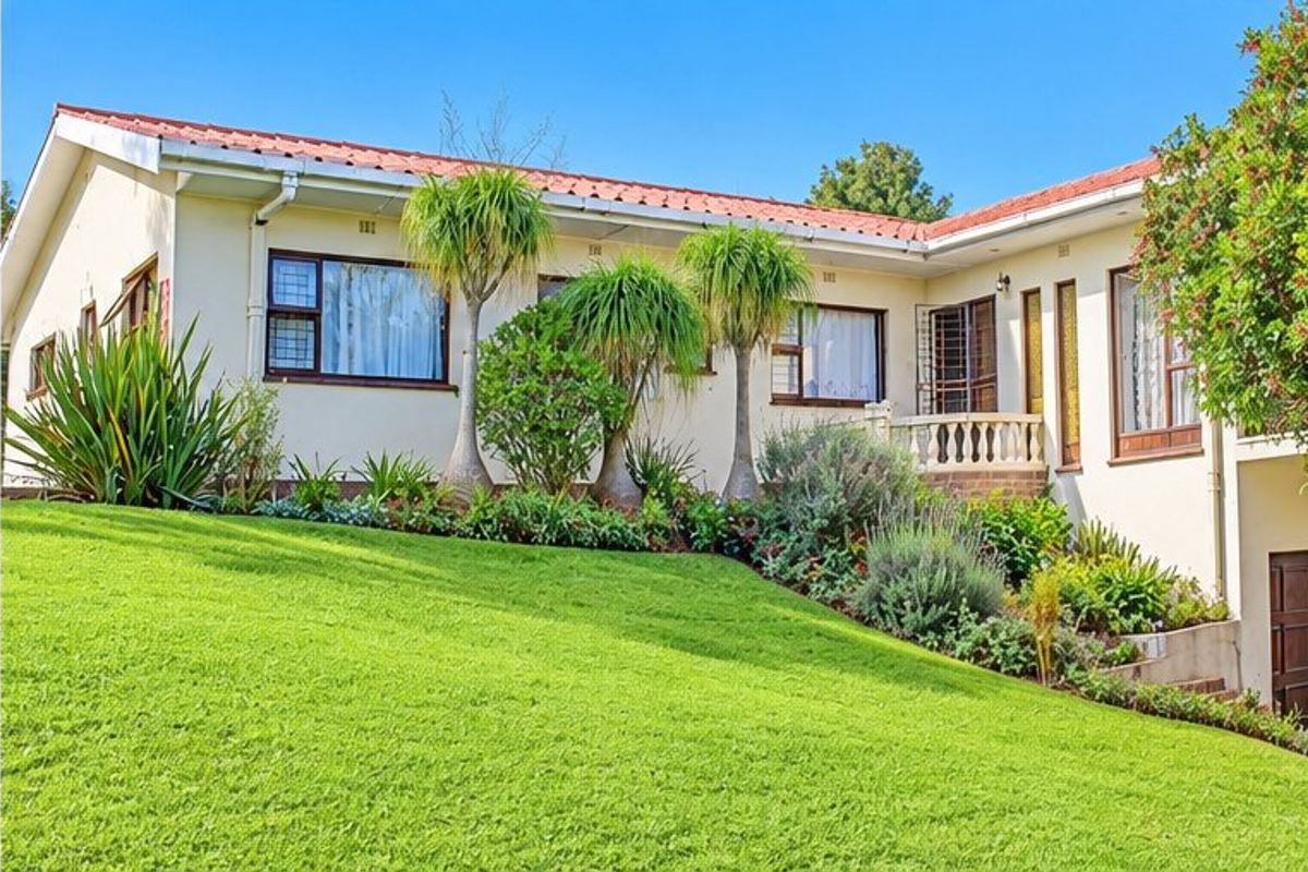 A well-maintained rear exterior view of the house featuring a terracotta tiled roof, established garden, and a raised patio area with a balustrade.