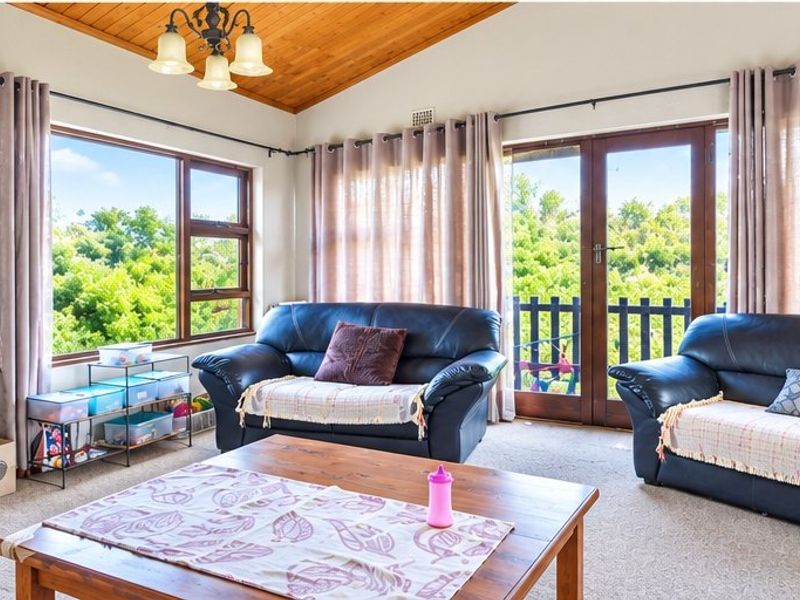 A bright living room featuring a vaulted timber-clad ceiling, large windows, and double glass doors providing access to an outdoor area.