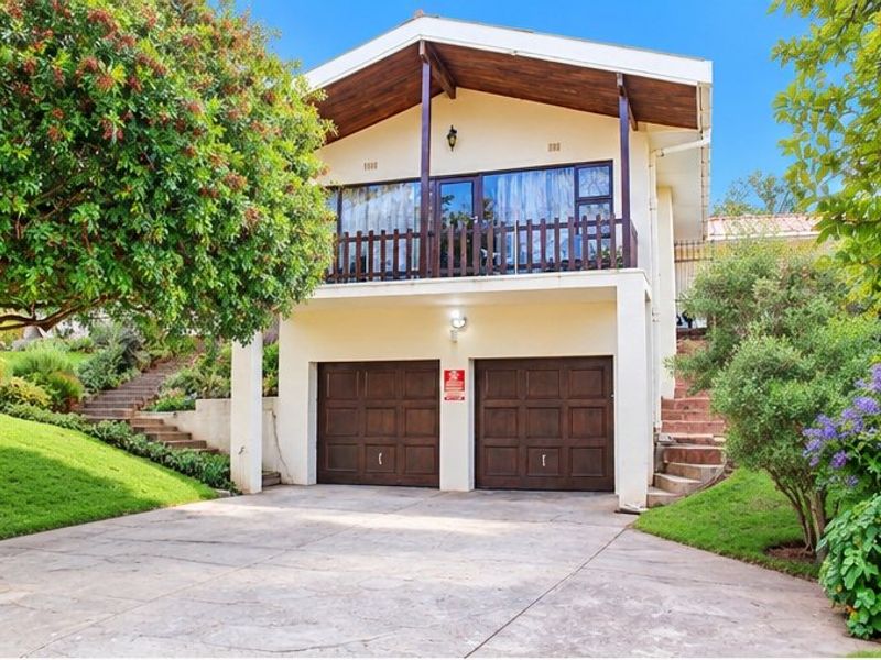 Front elevation of a two-story house featuring a double garage with timber doors and an upper-level balcony with wooden balustrades.