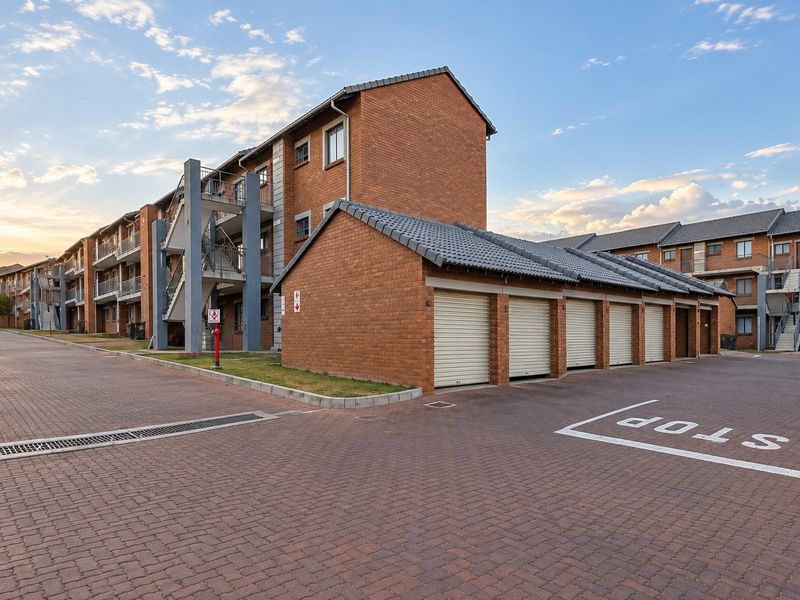 Exterior view of a multi-story apartment complex featuring brick construction, a row of garages, and paved driveway access.