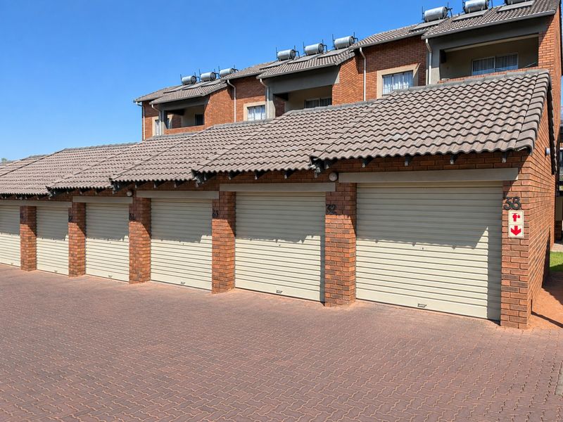 A row of brick-faced garages with roller shutter doors and a paved driveway, featuring solar water heaters installed on the roof.