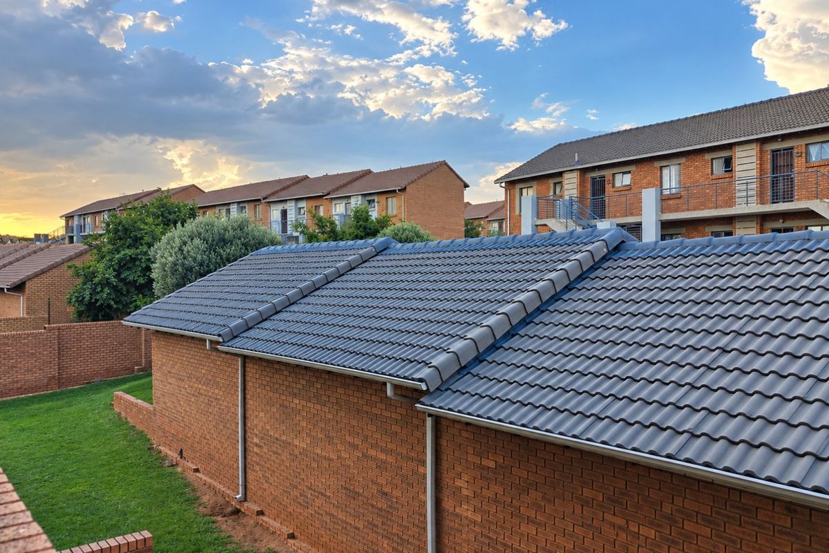 View of the rear exterior of the apartment complex, featuring brick construction, tiled roofing, and well-maintained communal lawn areas.