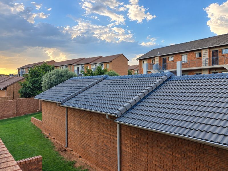 View of the rear exterior of the apartment complex, featuring brick construction, tiled roofing, and well-maintained communal lawn areas.