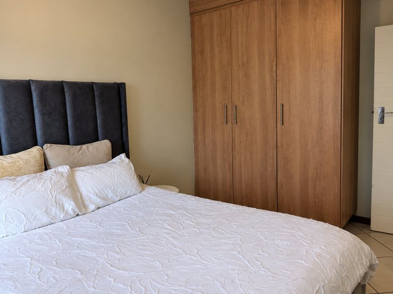 A well-maintained bedroom featuring neutral wall tones, tiled flooring, and a large built-in wooden wardrobe.