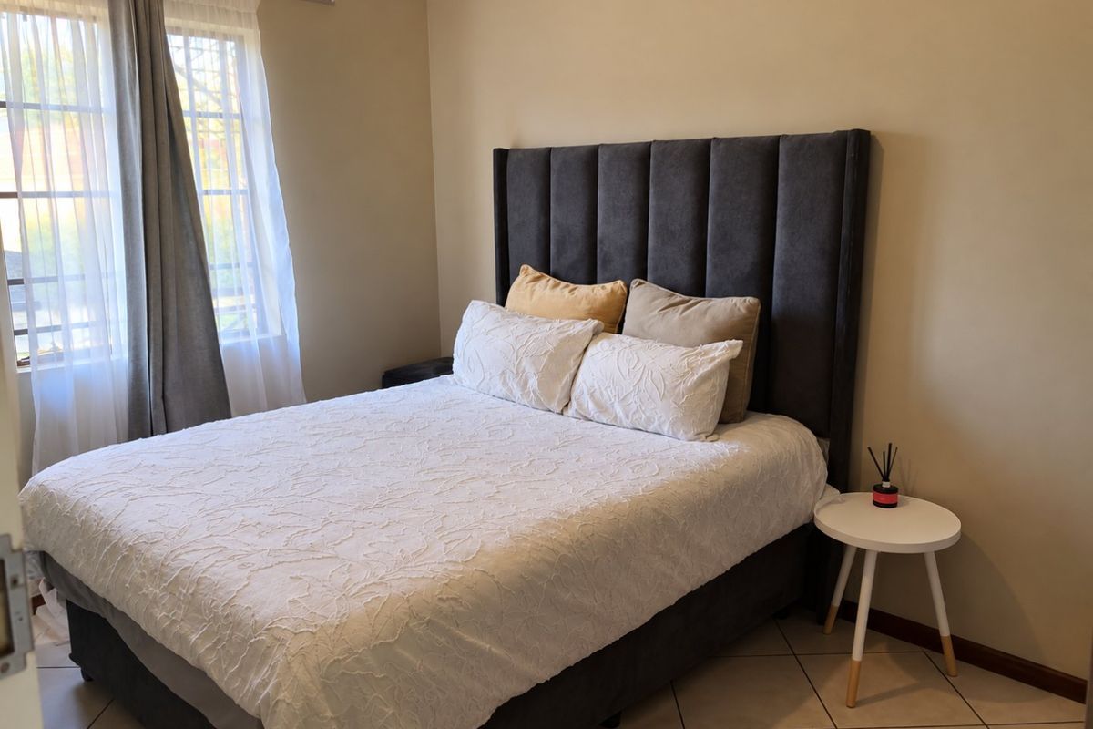A well-maintained bedroom featuring neutral wall tones, tiled flooring, and a large window allowing natural light.