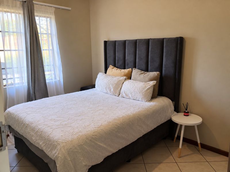 A well-maintained bedroom featuring neutral wall tones, tiled flooring, and a large window allowing natural light.
