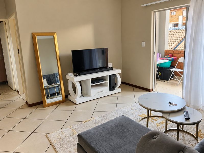 A well-maintained living room featuring tiled flooring and a sliding glass door providing access to an outdoor balcony area.