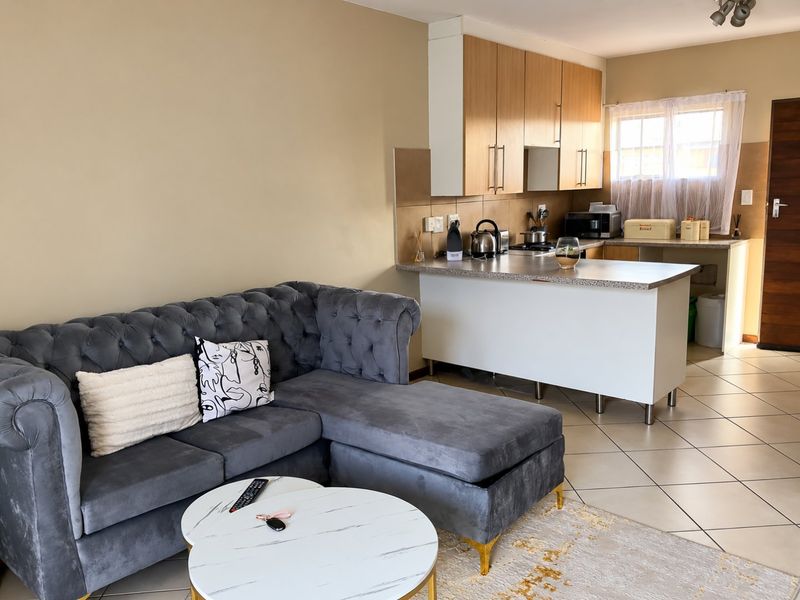 Open-plan living area featuring a functional kitchen with laminate cabinetry, tiled backsplash, and ceramic flooring, seamlessly connected to the lounge space.