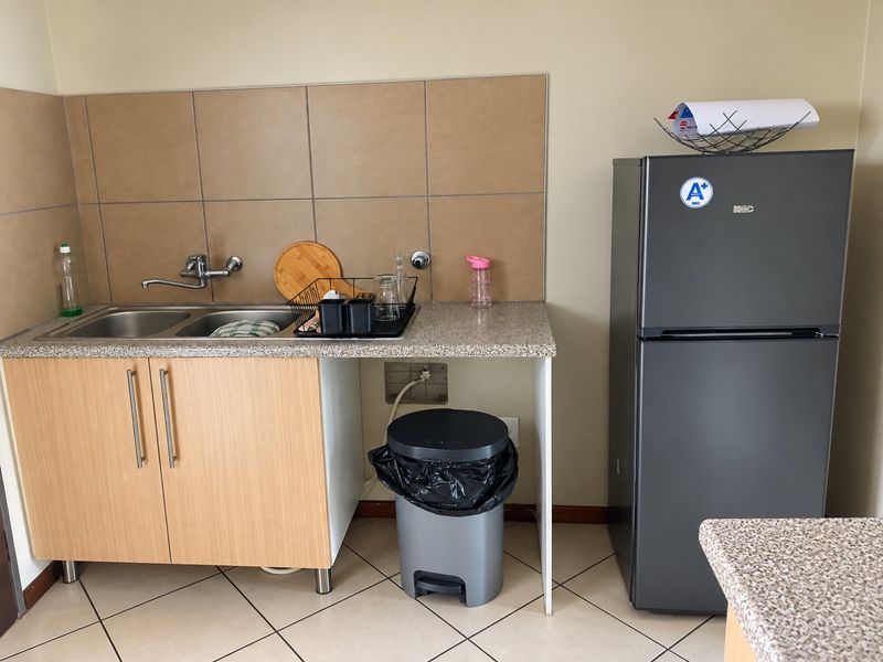 A compact kitchen area featuring a double bowl sink, laminate cabinetry, tiled splashback, and neutral floor tiles.
