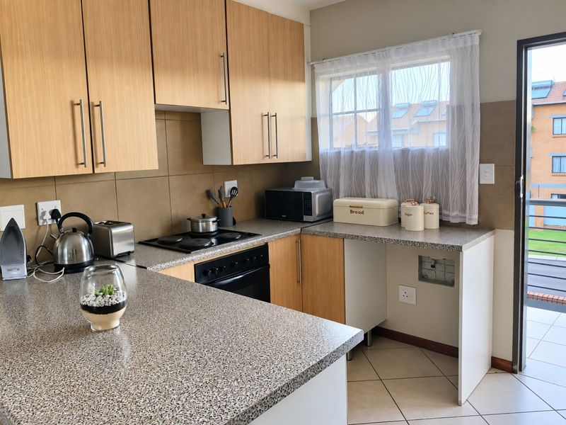 Functional kitchen featuring light wood-finish cabinetry, granite-look laminate countertops, built-in oven and hob, and direct access to an outdoor balcony area.