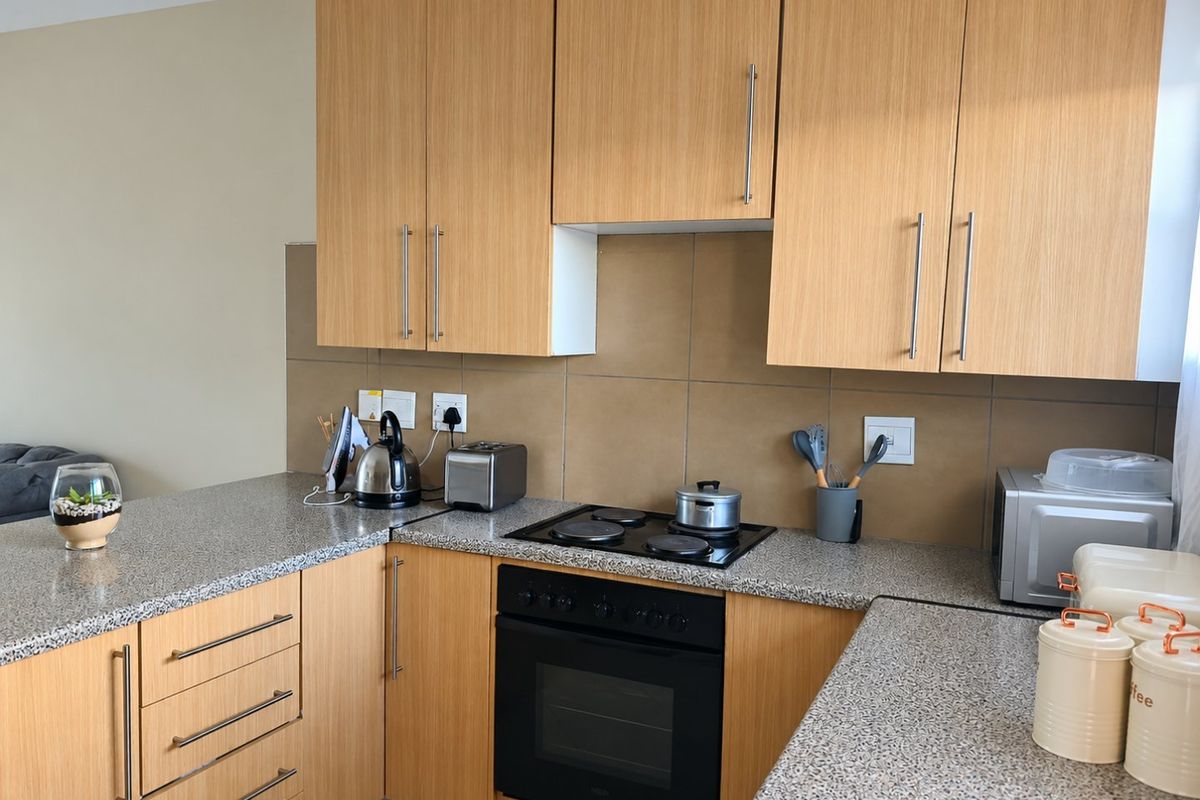 A functional kitchen featuring light wood-finish cabinetry, granite countertops, a tiled backsplash, and integrated electric cooking appliances.