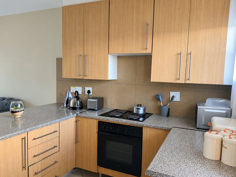 A functional kitchen featuring light wood-finish cabinetry, granite countertops, a tiled backsplash, and integrated electric cooking appliances.