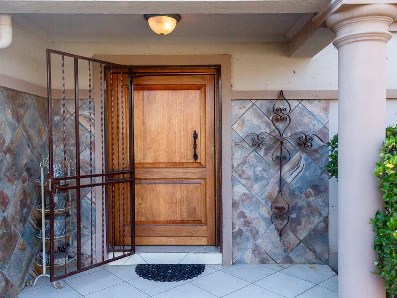 A covered entrance featuring a solid wood front door, protective metal security gate, and decorative tiled wall accents.