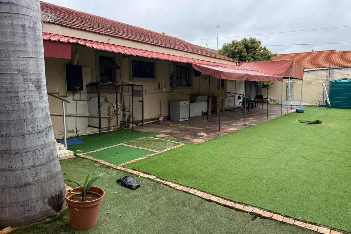 Rear exterior view of the property featuring a paved patio area, fixed awning, artificial lawn, and a water storage tank.