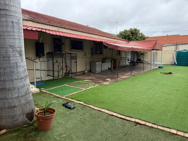 Rear exterior view of the property featuring a paved patio area, fixed awning, artificial lawn, and a water storage tank.