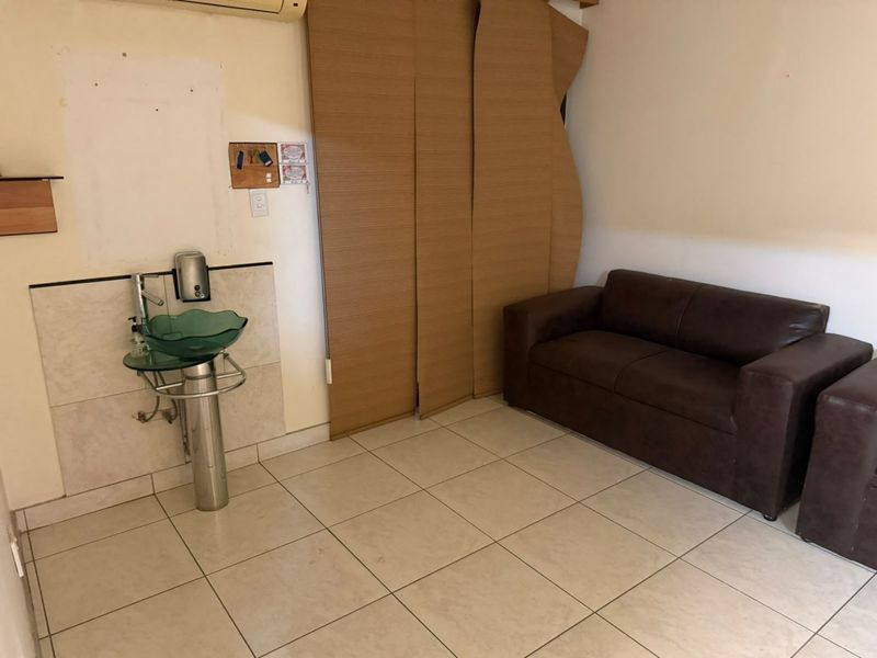 A utility space featuring tiled flooring, a pedestal washbasin, and wall-mounted air conditioning, currently showing signs of wear and damaged wall finishes.