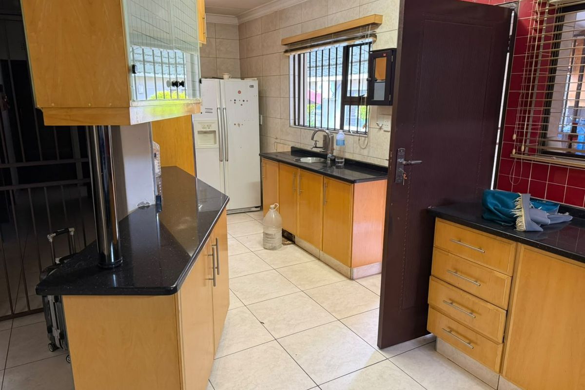 A functional kitchen featuring wooden cabinetry, granite countertops, tiled flooring, and a tiled backsplash with security bars on the windows.