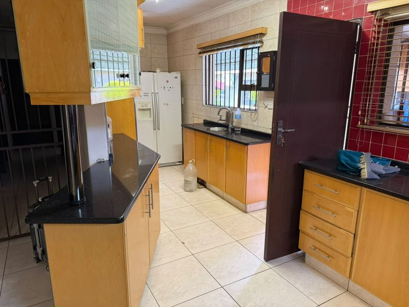 A functional kitchen featuring wooden cabinetry, granite countertops, tiled flooring, and a tiled backsplash with security bars on the windows.