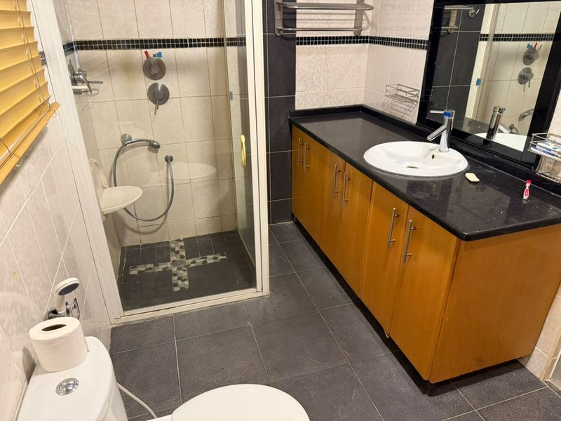 A functional bathroom featuring a shower enclosure, a vanity cabinet with a granite countertop, and tiled finishes throughout.