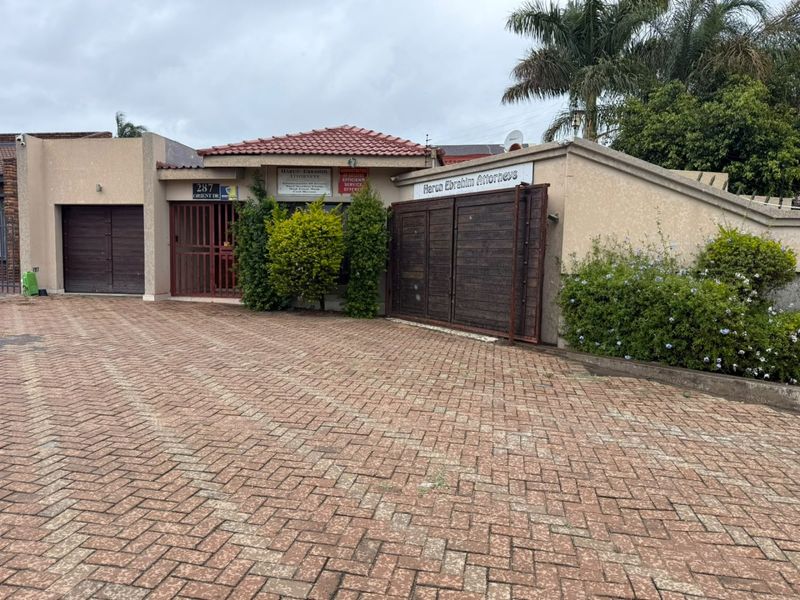 Front exterior view of the property featuring a paved driveway, garage access, and secure boundary walling with signage.