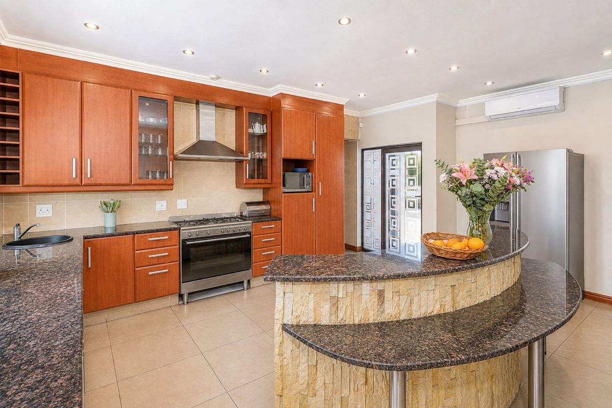 Spacious kitchen featuring warm wood cabinetry, granite countertops, a split-level breakfast bar with stone cladding, and integrated stainless steel appliances.