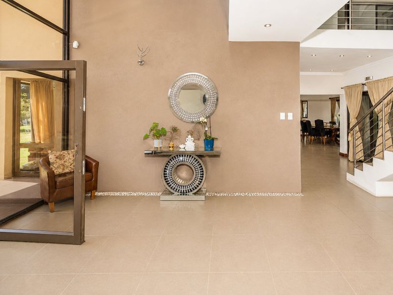 Spacious entrance hall featuring large format floor tiles, a modern staircase with metal balustrades, and a double-volume ceiling leading into the open-plan living area.