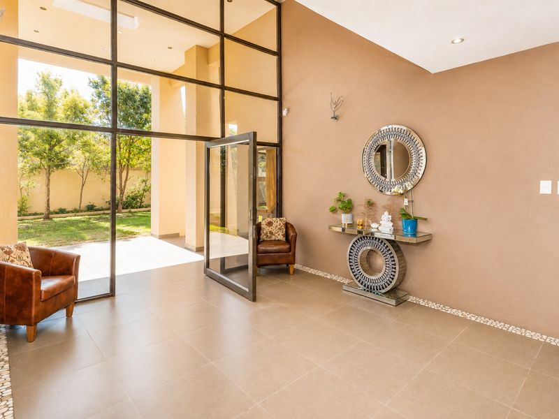 Spacious entrance hall featuring large floor-to-ceiling glass panels, tiled flooring with pebble border detailing, and recessed lighting, offering a bright and welcoming transition space.