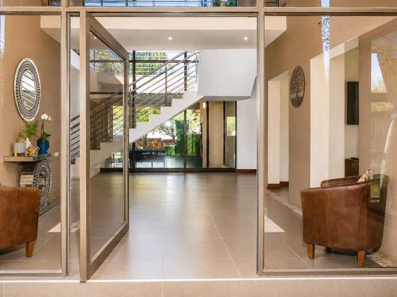 Spacious double-volume entrance hall featuring tiled flooring, a modern staircase with metal balustrades, and large glass pivot doors.