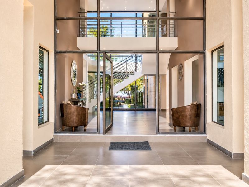 Grand entrance foyer featuring a large glass pivot door, modern tiled flooring, and a striking steel staircase with stainless steel balustrades.