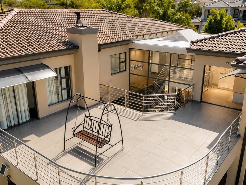 Spacious elevated balcony featuring tiled flooring, stainless steel railings, and a glass atrium overlooking the interior staircase.