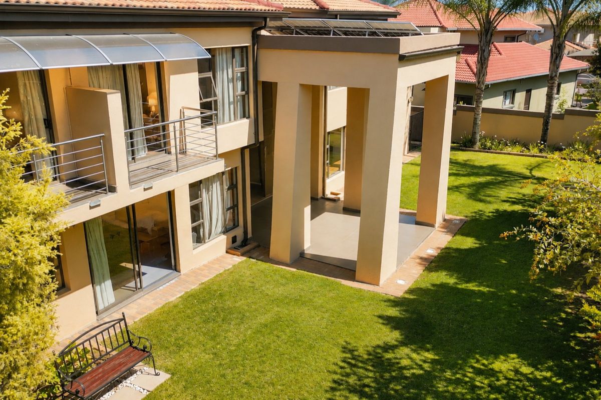 Rear view of a two-story residence featuring a covered patio, upper-level balcony with stainless steel railings, and a well-maintained garden.