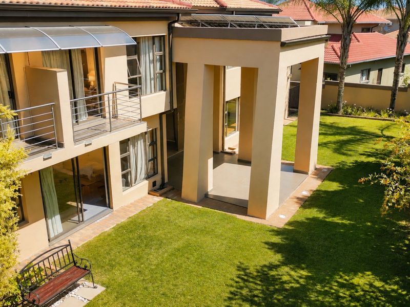 Rear view of a two-story residence featuring a covered patio, upper-level balcony with stainless steel railings, and a well-maintained garden.