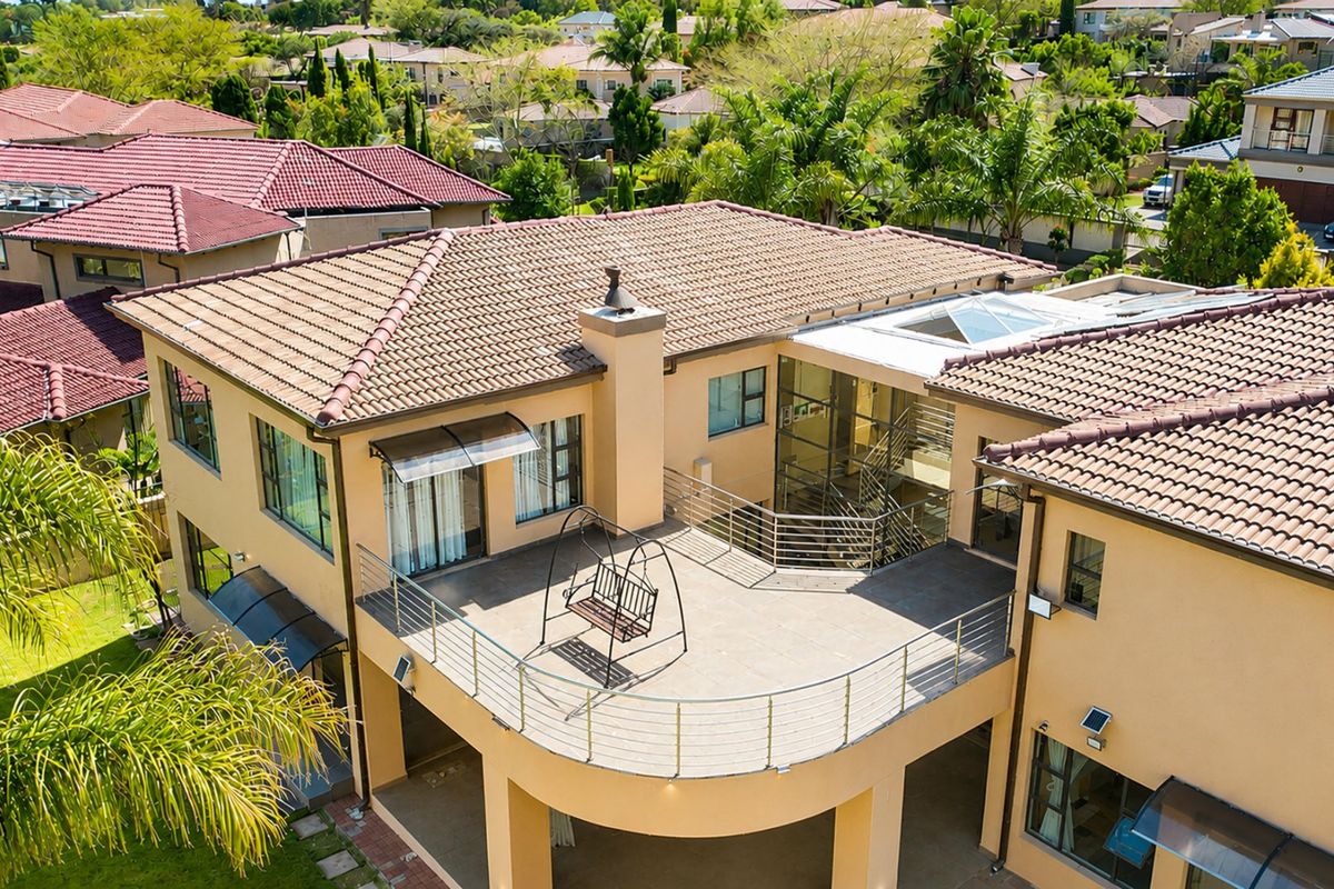 Aerial view of a multi-story residential property featuring a large tiled roof, a spacious balcony with stainless steel railings, and a modern glass-enclosed staircase.