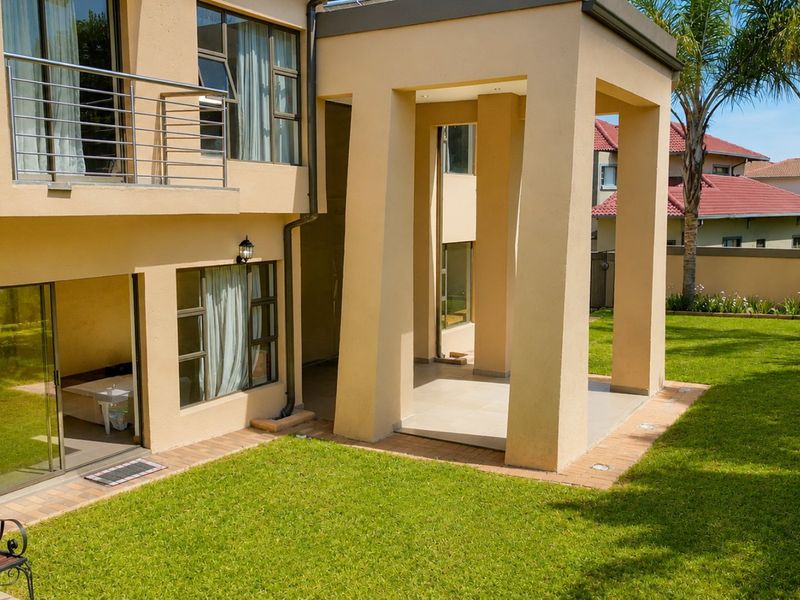 Rear view of the property featuring a covered patio, upper-level balcony with stainless steel railings, sliding glass doors, and a well-maintained garden.