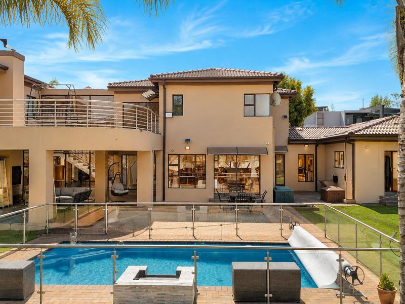 Spacious rear exterior featuring a swimming pool with glass fencing, a paved patio area, and an elevated balcony overlooking the garden.