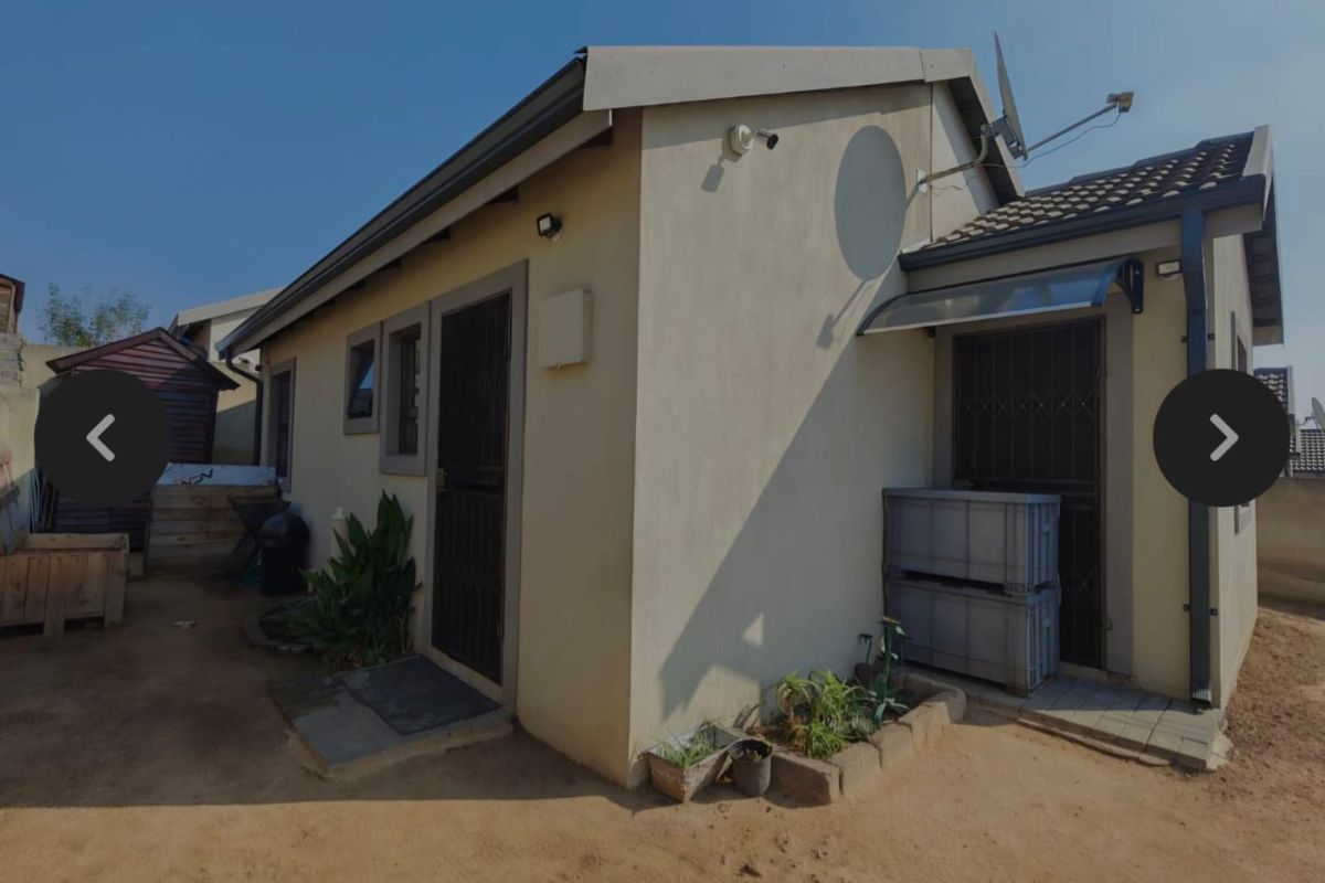 Rear exterior view of the property featuring a paved walkway, security gates, and installed satellite dish.