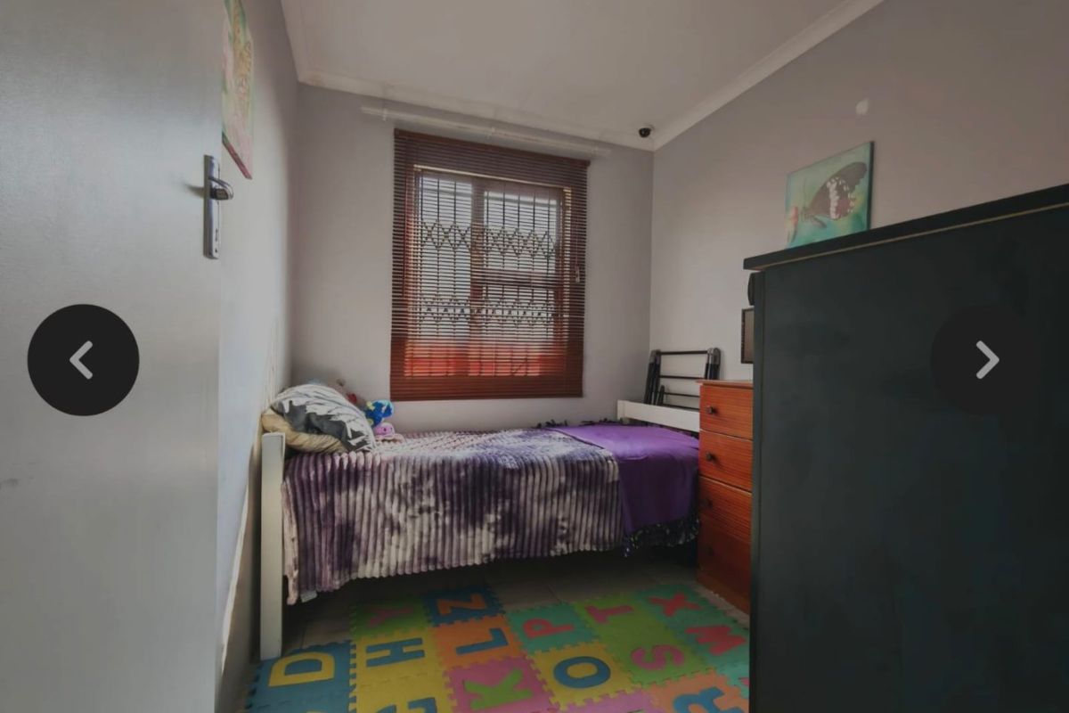 A compact bedroom featuring a window with venetian blinds and security gate, finished with neutral wall paint and coving.