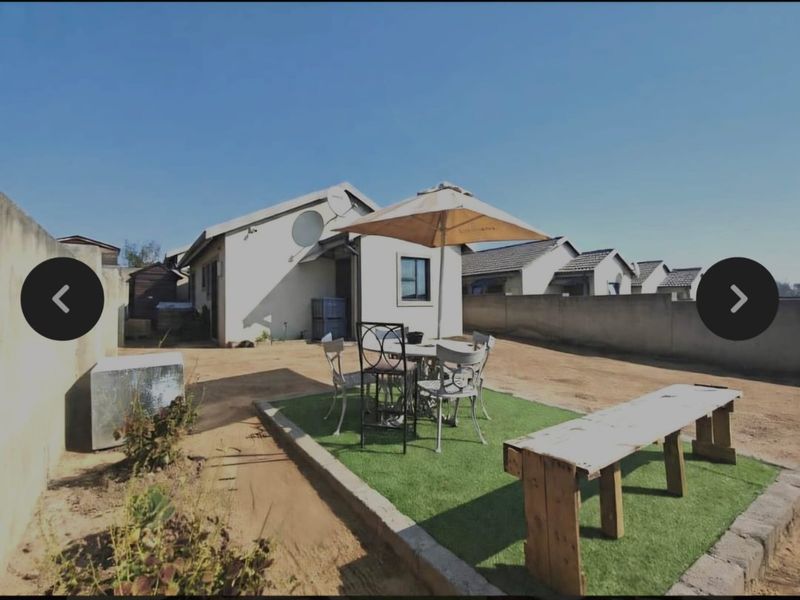 Rear exterior view of the property featuring a small artificial grass area, boundary walls, and an open yard space.