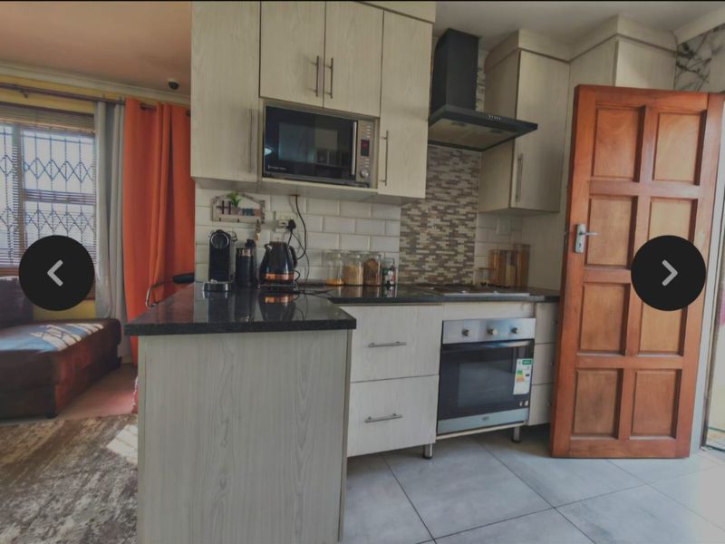 A compact, modern kitchen featuring light wood-finish cabinetry, granite countertops, a built-in oven with extractor fan, and a stylish subway and mosaic tile backsplash.
