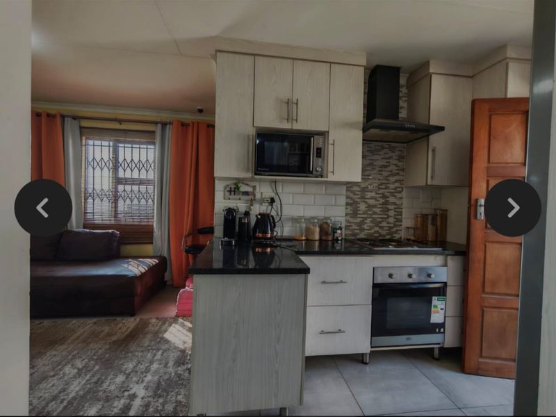 Open plan kitchen featuring light wood cabinetry, granite countertops, built-in oven, and extractor fan, seamlessly flowing into the adjacent living area.