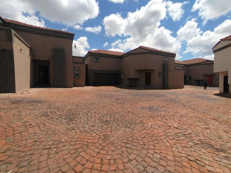 A wide-angle view of the property's front exterior, featuring a large cobblestone driveway and multiple building facades with tiled roofing.