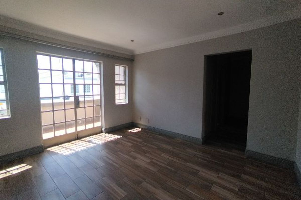 A bright, empty living room featuring wood-look tile flooring, recessed lighting, and a sliding glass door providing access to an outdoor area.