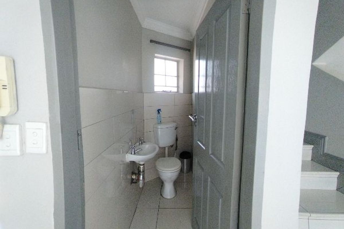 A compact guest bathroom featuring a wall-mounted basin, toilet, and neutral tiled finishes, located conveniently near the staircase.