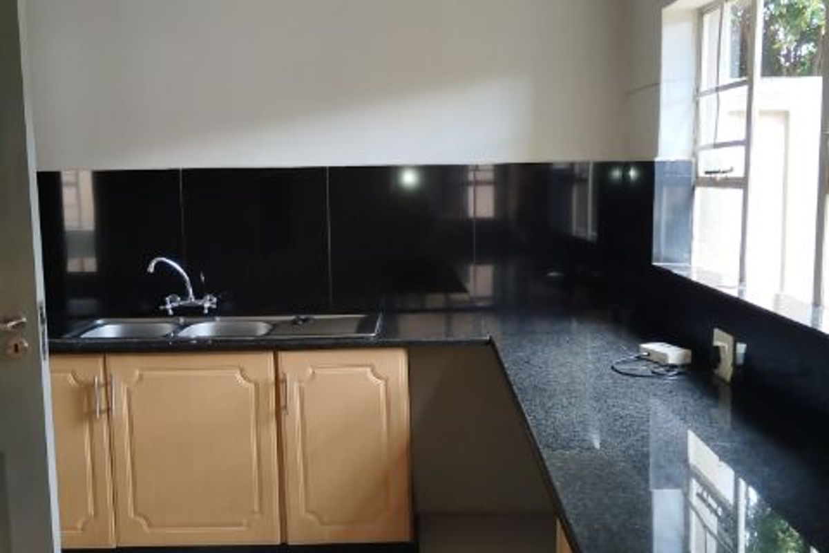 A clean, functional kitchen featuring granite countertops, double sink, and light wood cabinetry with a neutral tiled floor.