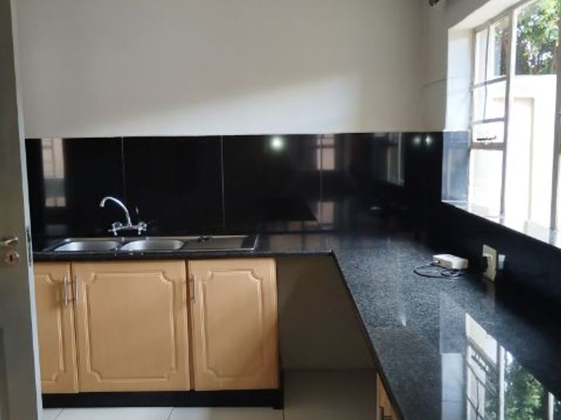 A clean, functional kitchen featuring granite countertops, double sink, and light wood cabinetry with a neutral tiled floor.