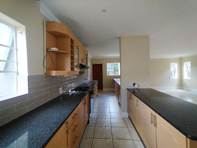 Spacious open-plan kitchen featuring granite countertops, wooden cabinetry, and tiled flooring, seamlessly flowing into the adjacent living area.