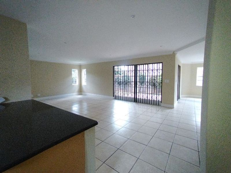 Spacious open-plan living area featuring neutral tiled flooring, recessed lighting, and large sliding doors with security gates leading to the exterior.