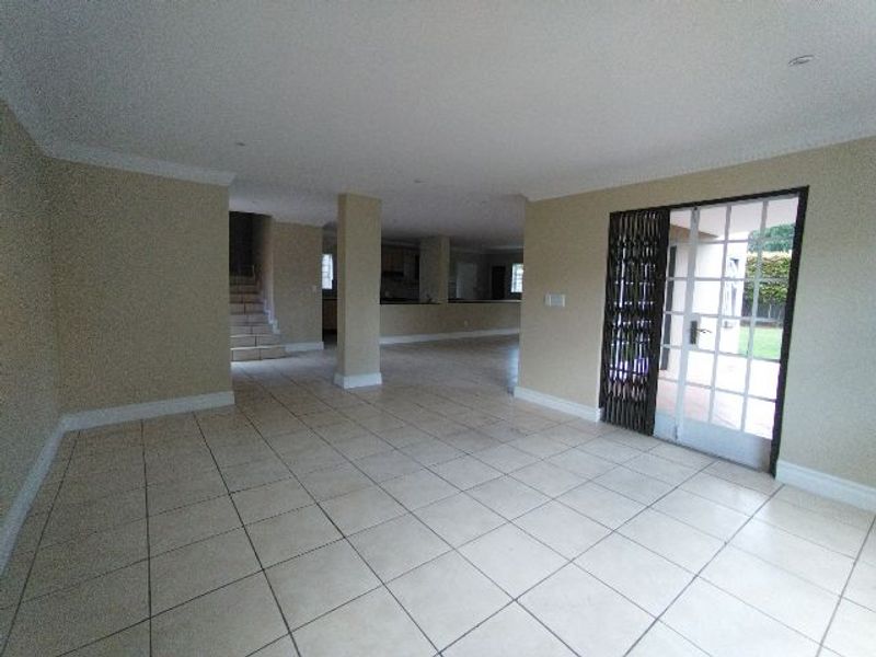 Spacious open-plan living area featuring neutral tiled flooring, recessed lighting, and direct access to the outdoor patio through a secure glass door.