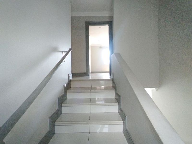 A bright, tiled staircase with a metal handrail leading to an upper level landing and doorway.