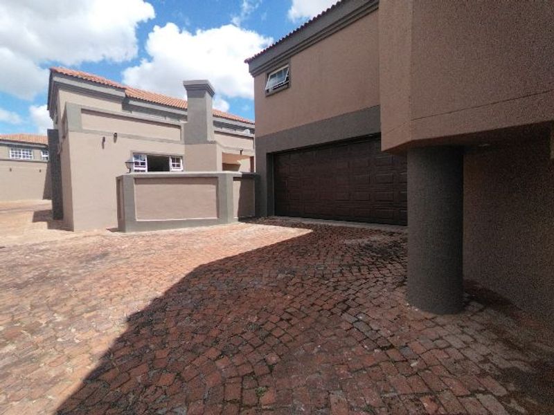 Front exterior view of the property featuring a cobblestone driveway, double garage, and plastered facade under a tiled roof.